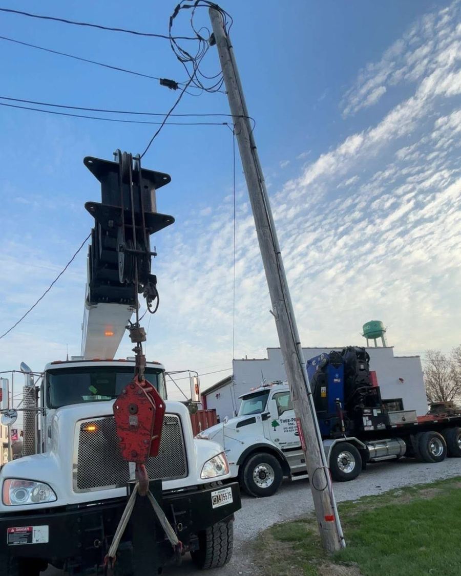 Tree Pros boom trucks performing a tandem lift over a street